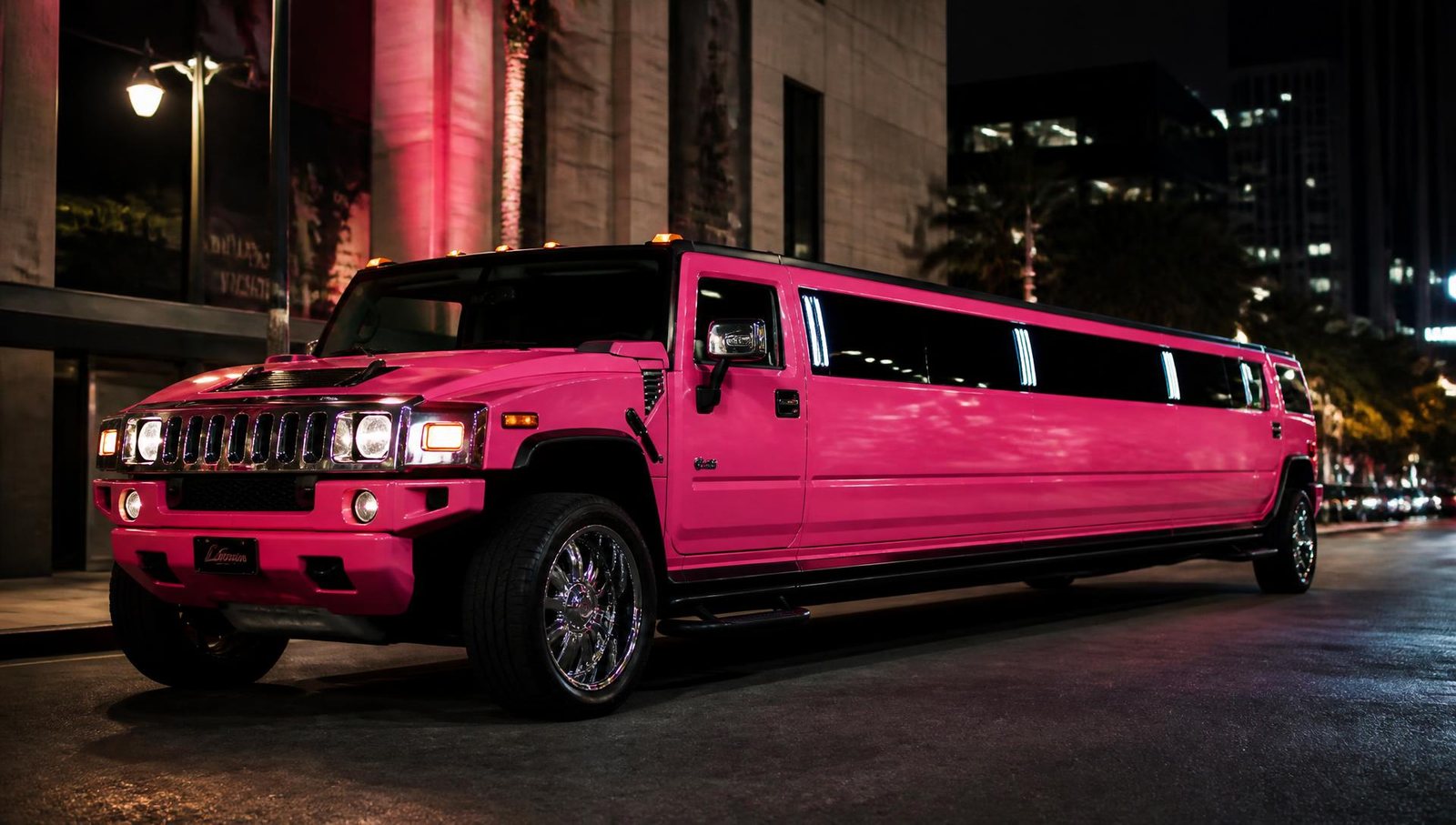 Pink Hummer H2 stretch limousine on a lit city street at night