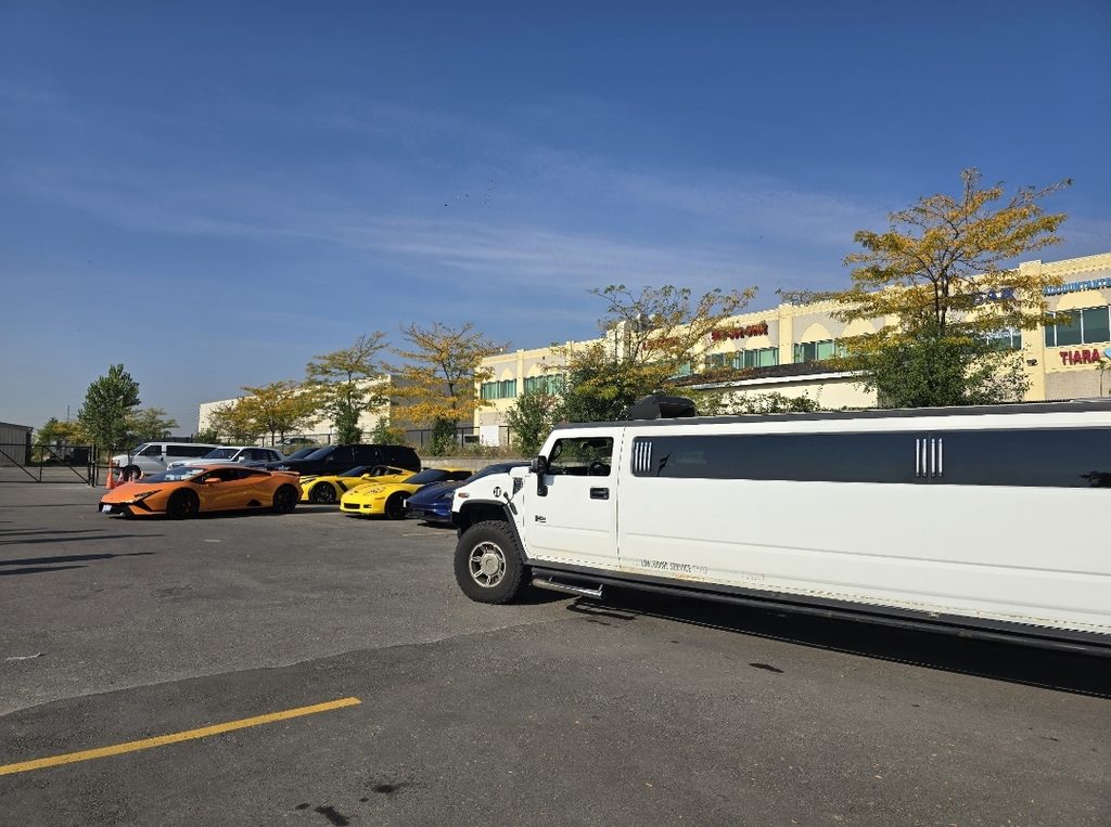 White Hummer stretch limousine alongside exotic sports cars on a sunny day